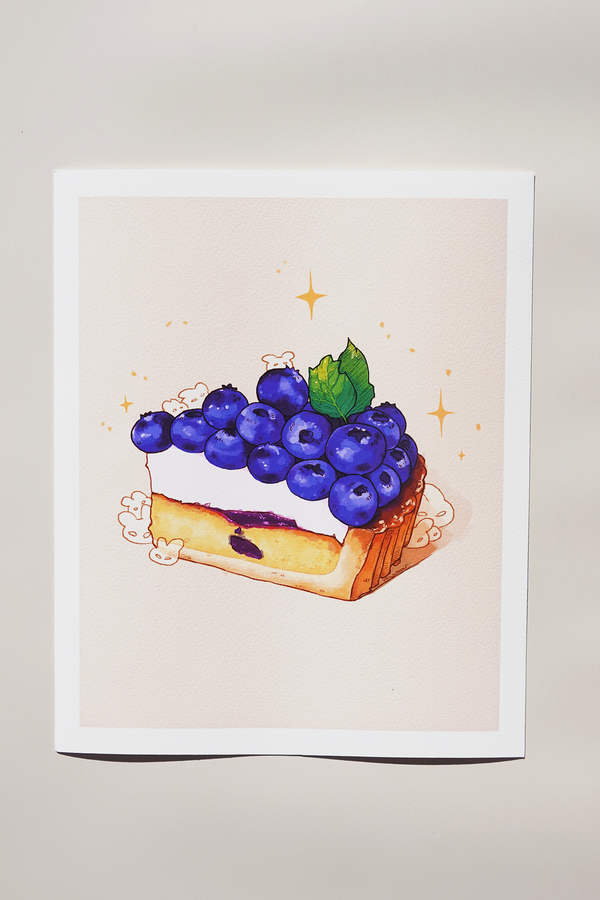 Art print of a blueberry tart illustration with whipped cream and mint leaf on top, surrounded by sparkles and tiny bunny characters — printed on textured fine art paper and photographed in natural light