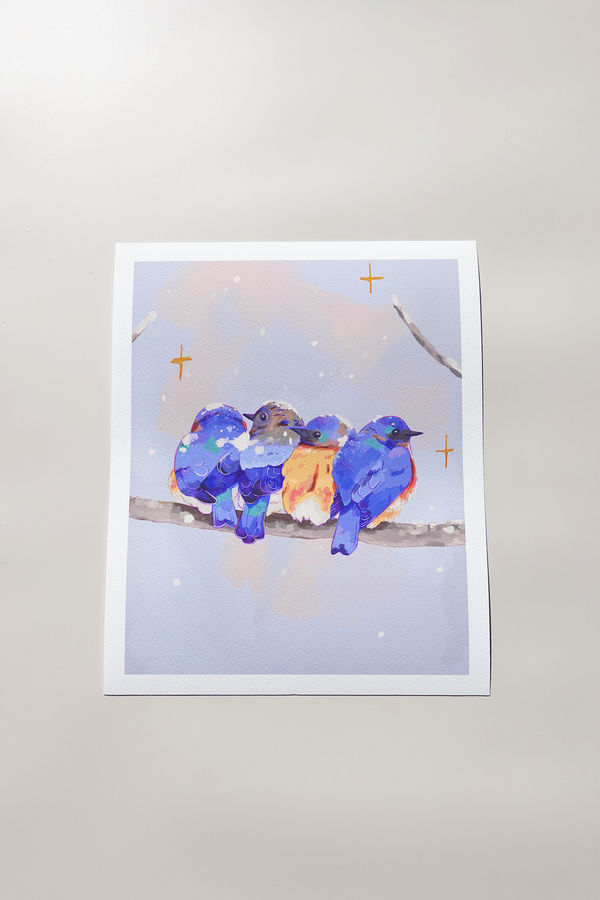 Art print of four plump bluebirds huddled together on a snowy branch, their vibrant blue and orange feathers contrasting a pastel winter sky — subtle sparkles dot the scene, printed on textured fine art paper