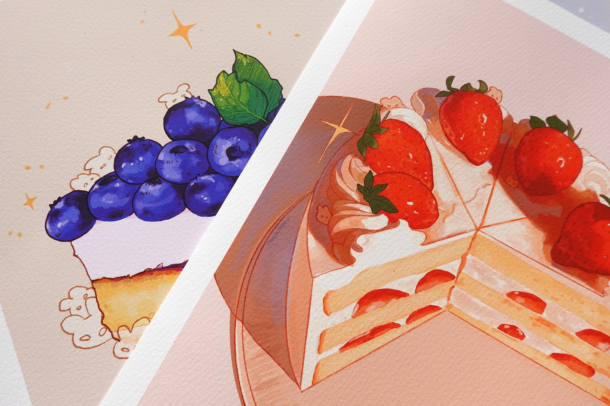Close-up of blueberry cheesecake and strawberry shortcake fine art prints on textured paper, featuring vibrant fruit toppings and hidden bunny characters in a painterly style — angled detail shot showing print quality and color richness for dessert-themed illustration decor